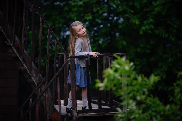 Une gentille petite fille se tient debout sur un escalier antique dans un village un soir d'été — Photo