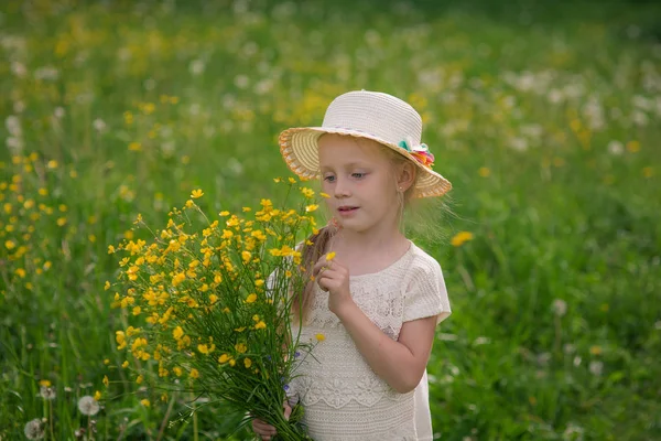 Mooie lachende blond kind meisje 4-5 jaar in de hoed met velden in het gebied met gele bloemen, met een boeket in handen — Stockfoto