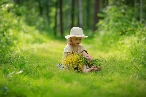 Uma menina de chapéu com um buquê de flores no caminho da floresta — Fotografia de Stock