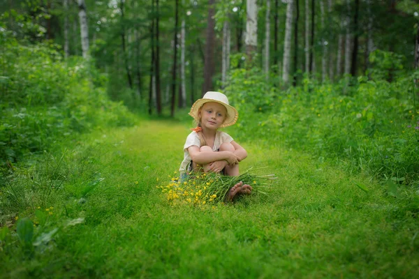 Una ragazza con un cappello con un mazzo di fiori su un sentiero nel bosco — Foto Stock