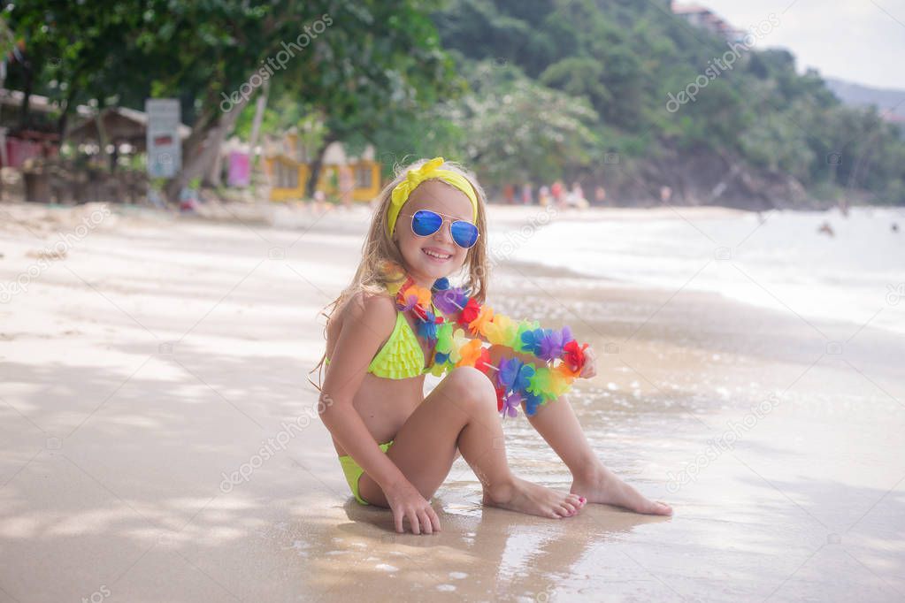 Happy little girl smiles in sunglasses on the beach at the seaside