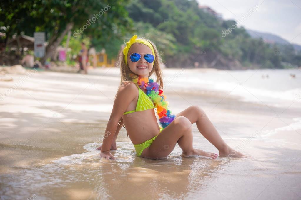 Happy little girl smiles in sunglasses on the beach at the seaside