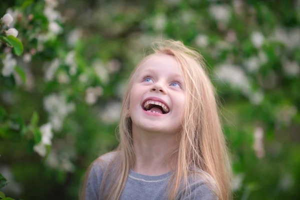 Een schattige mooie meisje met lang haar lacht naast een bloeiende boom in een park — Stockfoto