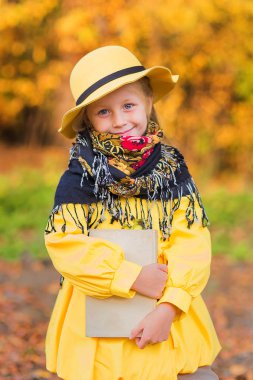 Portre sevimli güzel bir kızın sarı şapka ve sarı bir kat bir sonbahar Park onun elinde bir kitapla