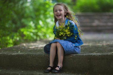 Bir buket çiçek ile bir parkta oturan tatlı, mutlu, gülümseyen altı yaşında bir kız. Yaz. Çocukluk. Tatil.