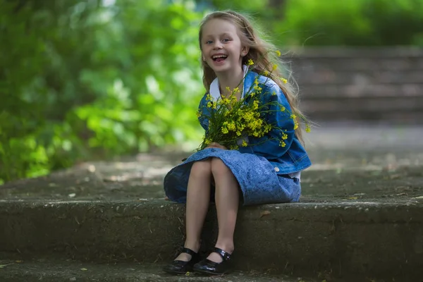 Милая, счастливая, улыбающаяся шестилетняя девочка, сидящая в парке с букетом цветов. Саммер. Детство. Праздники . — стоковое фото
