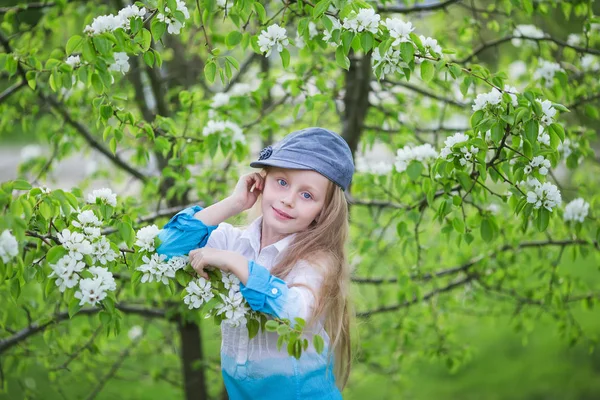 Portrait a beautiful little girl a flowering garden in the spring. Cute child with blond hair in a blooming garden — Stock Photo, Image