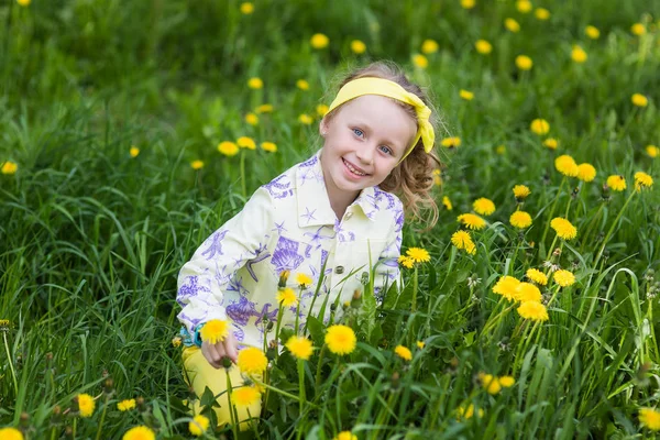 Una graziosa bambina ridente in un campo con i denti di leone — Foto Stock