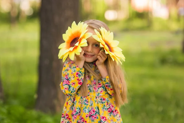 Meisje in park glimlachend en die betrekking hebben op gezicht met zonnebloem — Stockfoto