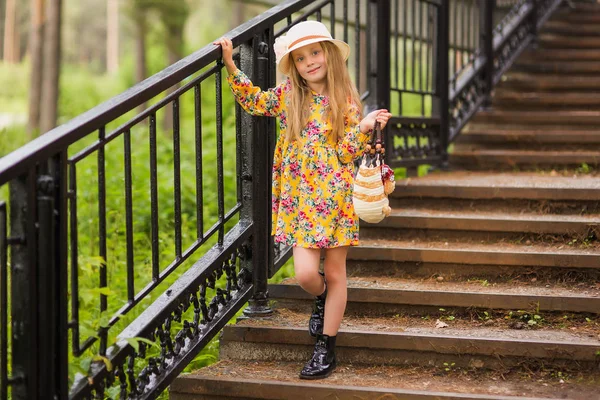 Menina elegante bonita doce em um chapéu e um saco até as escadas no parque . — Fotografia de Stock