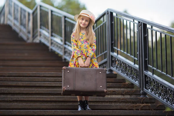 Menina doce em um chapéu com uma mala em pé nas escadas à espera — Fotografia de Stock