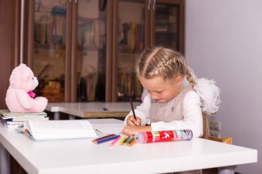 İki örgüler ile tatlı kız okul masasında dersler öğretir. oyuncak oyuncak ayı oturan