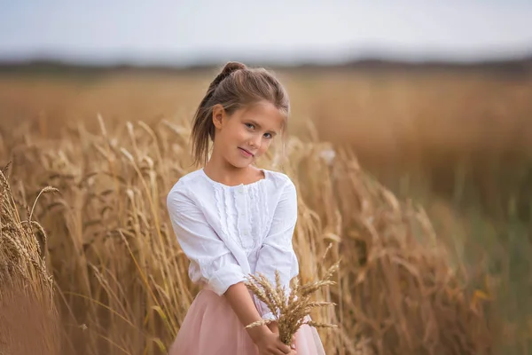 Retrato de uma menina bonita com cabelos longos com um buquê de trigo no campo de verão — Fotografia de Stock