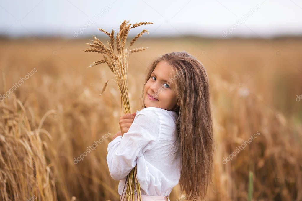 Portrait of a cute girl with long hair with a bouquet of wheat in the summer field