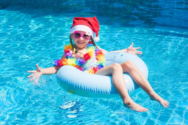 Noel Baba şapkalı küçük kız. Tropiklerde yüzme havuzunda tatilde. Tatil kavramı. Yeni yıl konsepti.