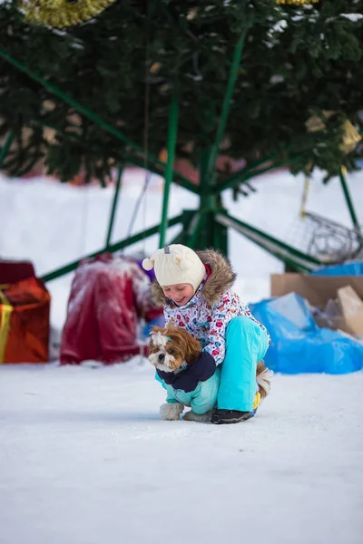 Happy little girl with a dog in overalls on a background of a Christmas tree on a winter frosty day