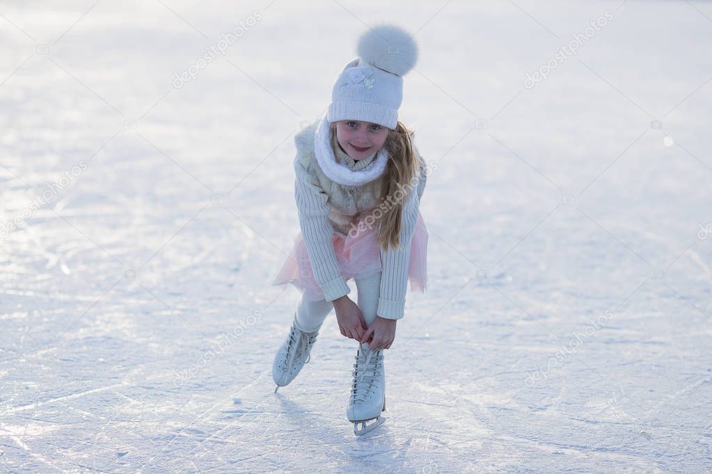 Adorable little girl in the white clothes and hat on the ice rink