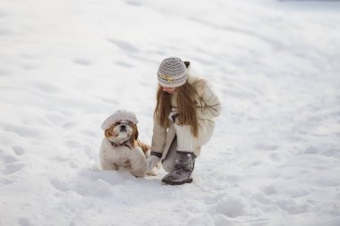 Güzel küçük kız kışın köpeğiyle parkta yürüyor.