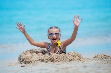 Kumsalda eğlenen bir çocuk, güneşli bir günde oynaşan sevimli bir kız, tropik bir plaj. Kum ve dalgalarla oynayan bir deniz.