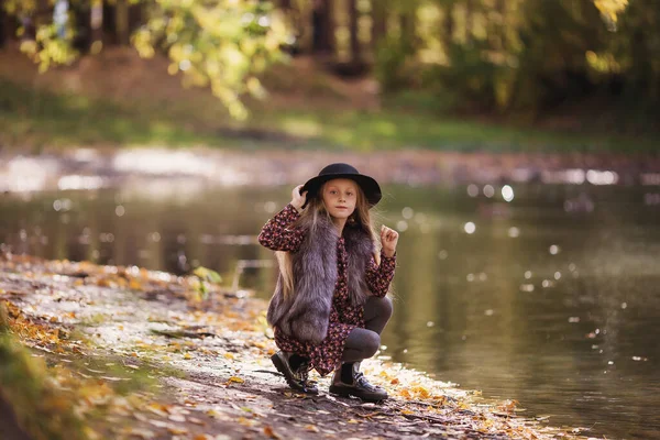 美しい笑顔ファッショナブルな女の子の肖像画 晴れた日に池のそばに長い髪の少女が座っている — ストック写真
