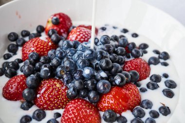 Çilek, yaban mersini ve beyaz bir kabın içinde süt