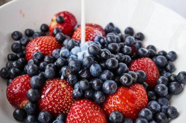 Çilek, yaban mersini ve beyaz bir kabın içinde süt