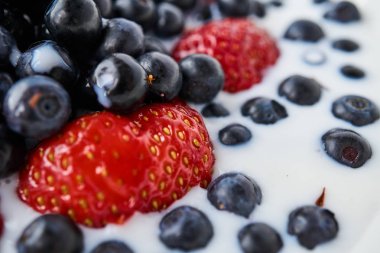 Çilek, yaban mersini ve beyaz bir kabın içinde süt