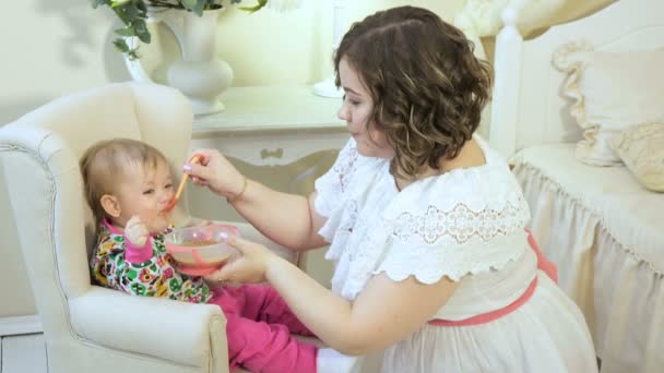 Красивая женщина в белом платье кормит маленького ребенка пюре — стоковое видео