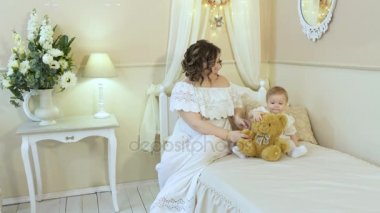 Anne ve küçük kızı yatağa oturmuş ve bir oyuncak ayı oynamak