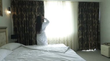 Güzel kız beyaz paltolu bir otel odasında penceresine gider