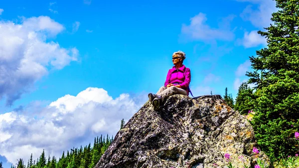 Donna anziana seduta su una grande roccia durante un'escursione al Monte Tod al villaggio Sun Peaks nelle Shuswap Highlands — Foto Stock