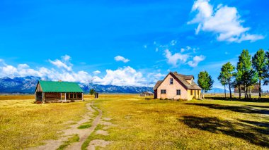 Mormon Row 'da terk edilmiş çiftlik evleri, arka planda bulutlarla kaplı Grand Tetons Tepeleri Grand Tetons Ulusal Parkı, Jackson Hole, Wyoming, ABD