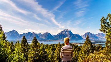 Woman enjoying the view of Jackson Lake and the tall mountain peaks of the Teton Range viewed from Signal Mountain in Grand Teton National Park in Wyoming, United States clipart