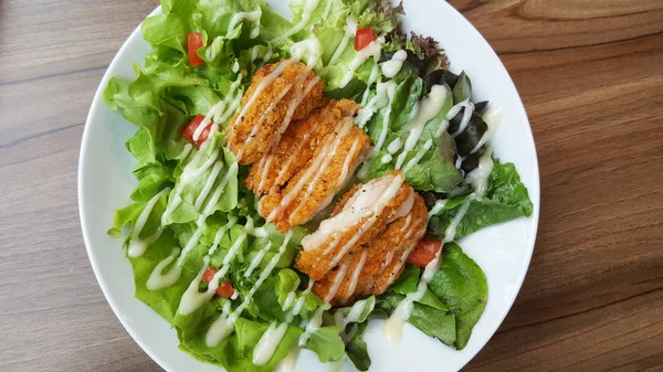 Breaded fried chicken with organic green caesar salad tomato on wooden table at western restaurant, food recipe menu advertisement