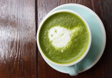 Çatı katı tarzı kahve dükkanının ahşap masasında, beyaz bardakta sütle süslenmiş kalp şeklinde sütlü kibrit yeşil çay lattesi, ticari reklam arka planı.