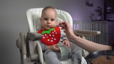 Dolly vurdu. Anne, bebek koltuğunda yakışıklı bebeği besliyor..
