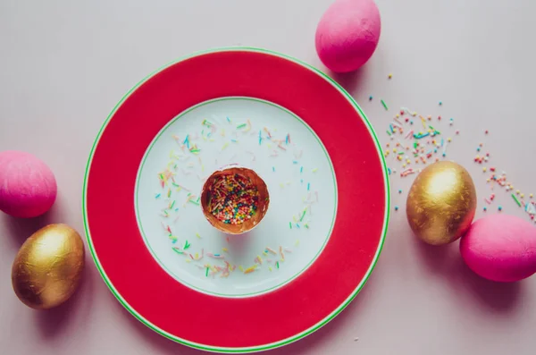 Oeufs de Pâques roses et dorés colorés avec des confiseries saupoudrer sur l'assiette — Photo