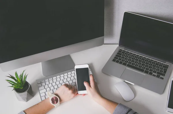 Mãos segurando smartphone e com diferentes dispositivos na mesa, mock up — Fotografia de Stock