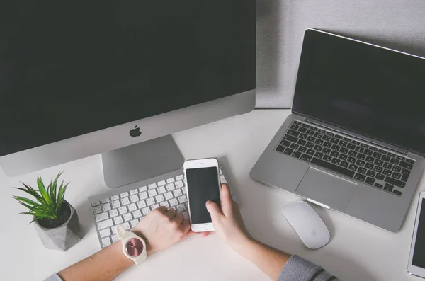 Mãos segurando iphone7 e diferentes dispositivos na mesa, mock up — Fotografia de Stock