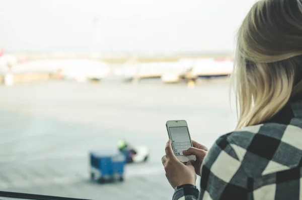 Young woman holding smartphone in airport — Stock Photo, Image