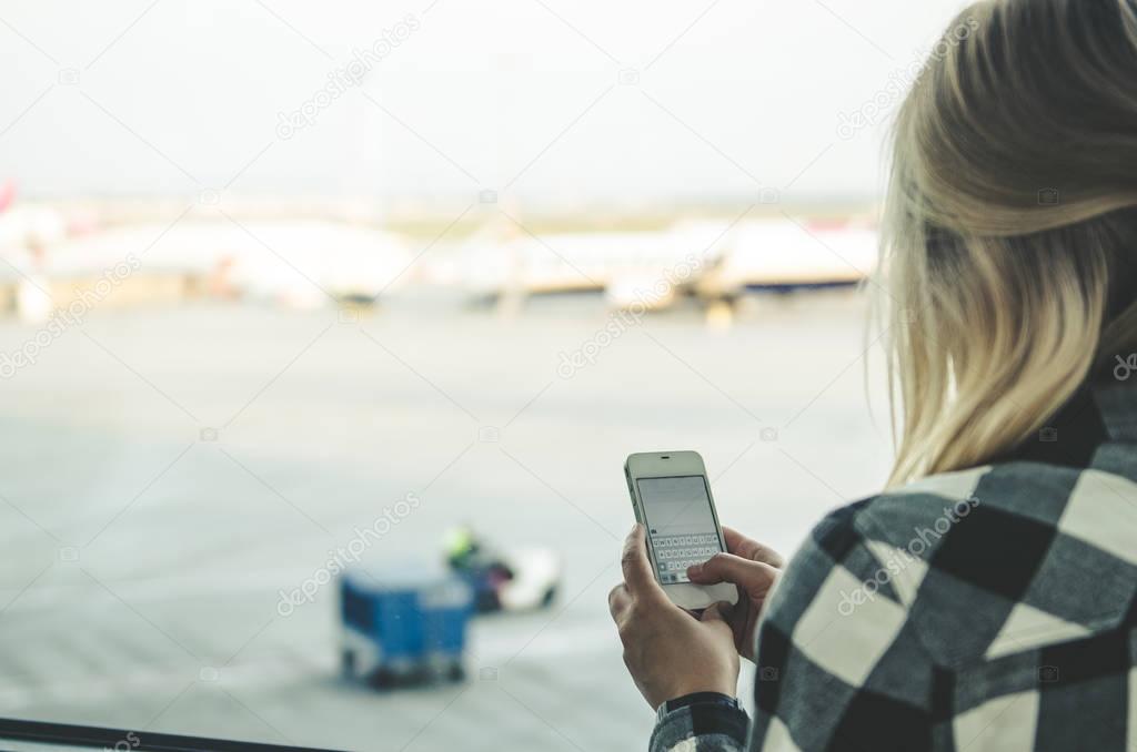 young woman holding smartphone in airport 