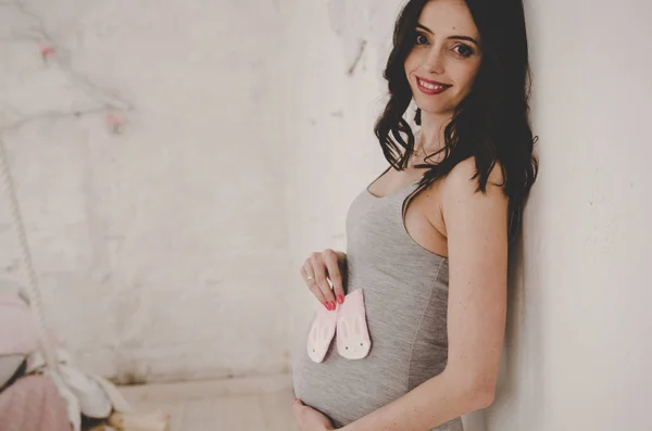 Gravid kvinna nära väggen och innehav baby Strumpor — Stockfoto