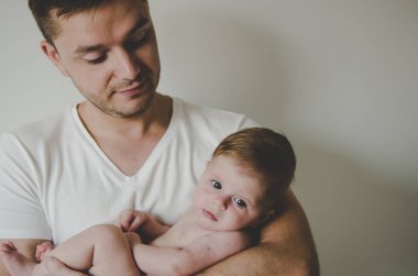 Genç ve yakışıklı baba küçük kızını elinde tutuyor ve beyaz arka planda şefkatle bakıyor. 
