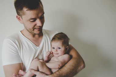 Genç ve yakışıklı baba küçük kızını elinde tutuyor ve beyaz arka planda şefkatle bakıyor. 