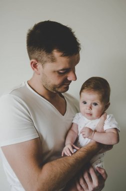 Genç ve yakışıklı baba küçük kızını elinde tutuyor ve beyaz arka planda şefkatle bakıyor. 