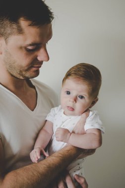 Genç ve yakışıklı baba küçük kızını elinde tutuyor ve beyaz arka planda şefkatle bakıyor. 