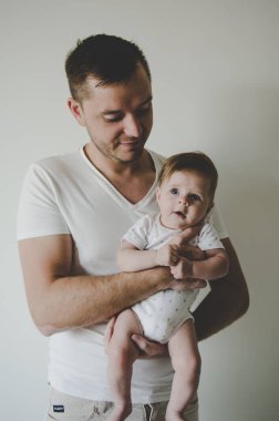 Genç ve yakışıklı baba küçük kızını elinde tutuyor ve beyaz arka planda şefkatle bakıyor. 