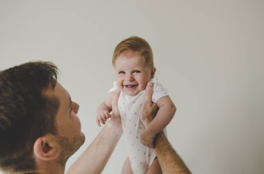 Babanın elinde beyaz arka plan üzerinde gülümseyen beyaz vücut elbiseli küçük bebek kız