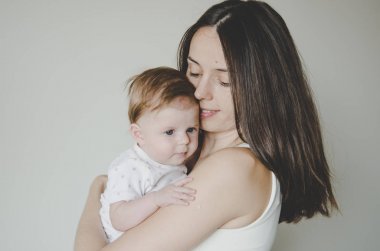 Genç ve güzel anne beyaz arka planda küçük kızına sarılıyor.