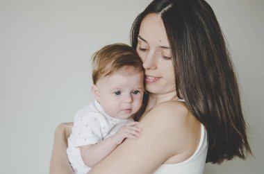 Genç ve güzel anne beyaz arka planda küçük kızına sarılıyor.